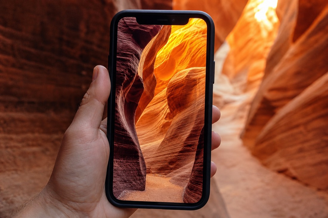 Phone screen framing a curved sandstone wave inside a glowing slot canyon