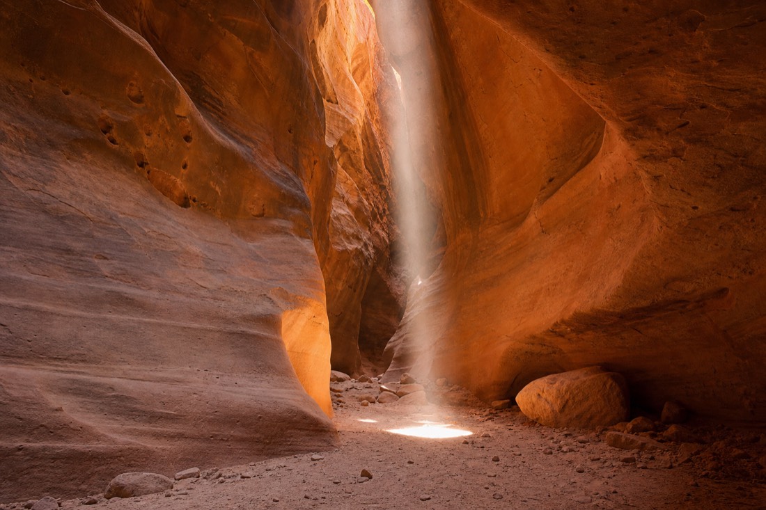 Vertical shaft of sunlight hitting the sandy floor of a slot canyon at midday
