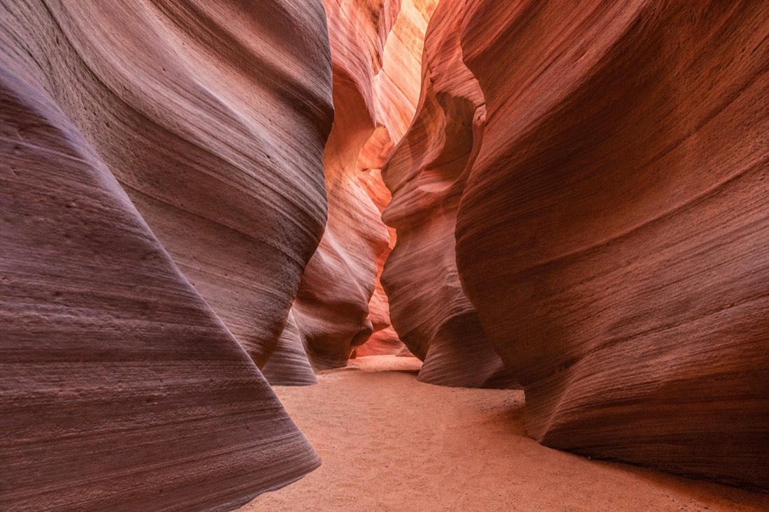 Quiet slot canyon corridor in soft light with undisturbed sand on the floor