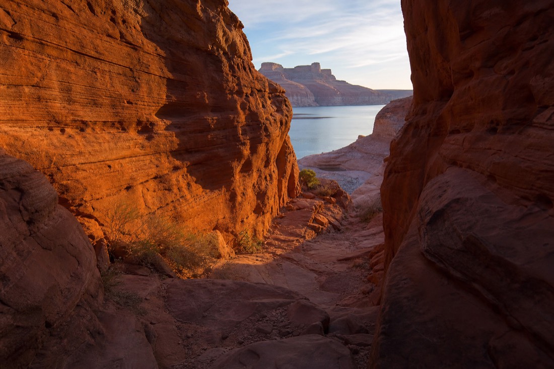 Morning light on a slot canyon entrance with a calm lake visible in the distance later in the day