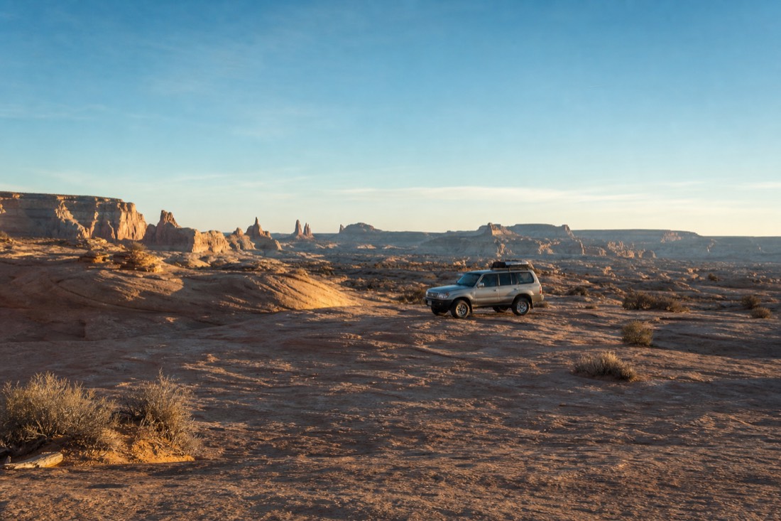 Early morning desert light over sandstone terrain with a single parked tour vehicle