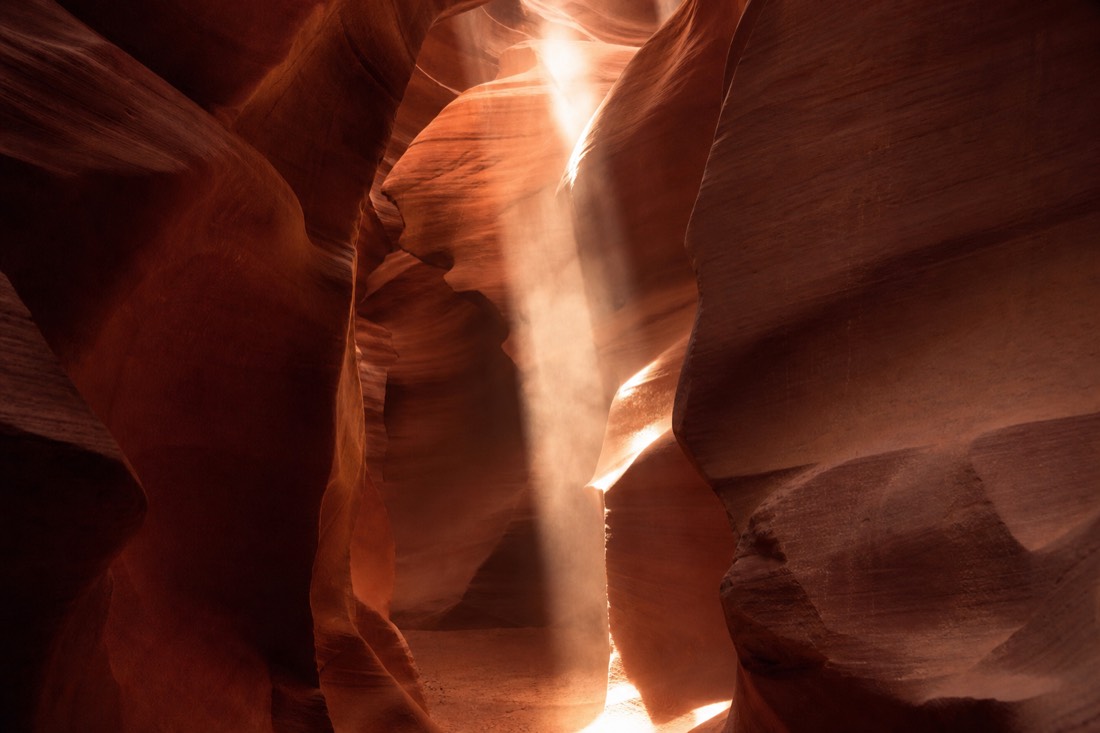 Bright vertical sunbeam cutting through dust inside a narrow sandstone slot canyon