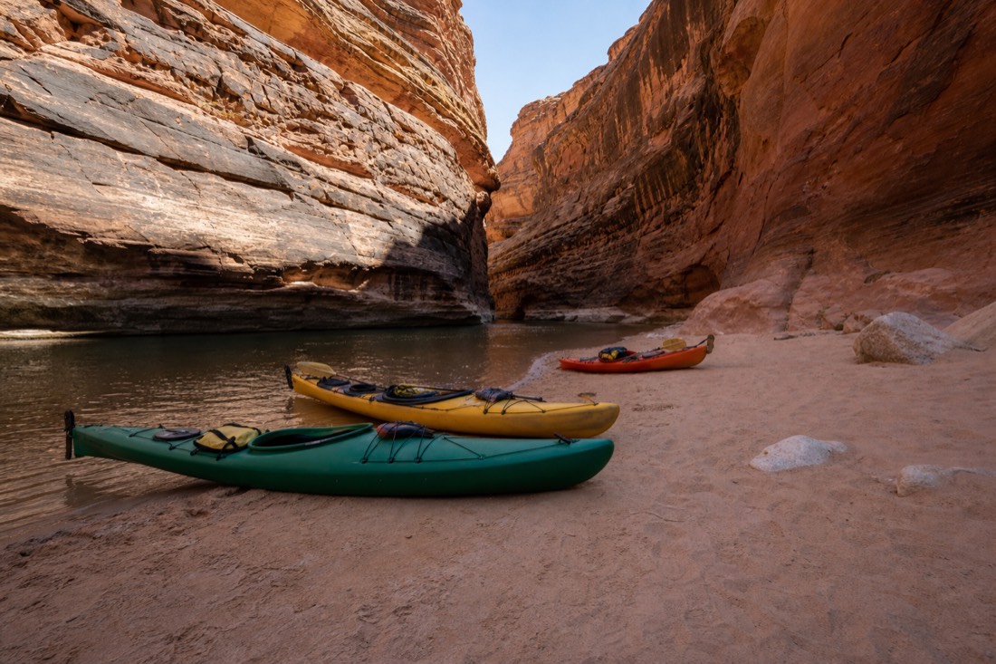 Small group of kayakers beaching their boats on sand where a canyon narrows above the waterline