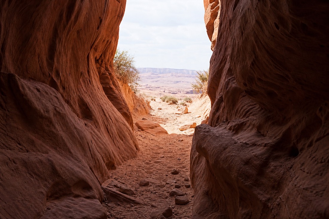 Slot canyon opening onto bright desert terrain near the Horseshoe Bend area