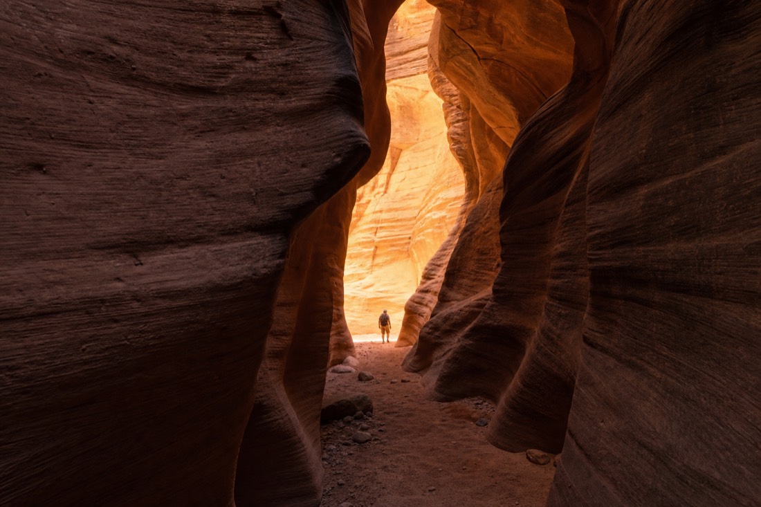 Single visitor silhouetted in a glowing empty slot canyon corridor