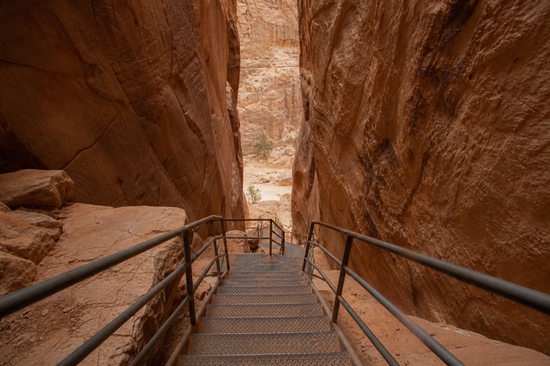 Steep metal staircase descending between tight sandstone walls into a slot canyon