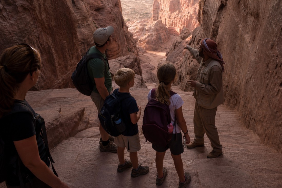 Family pausing at the top of a canyon staircase while a guide gestures toward the route