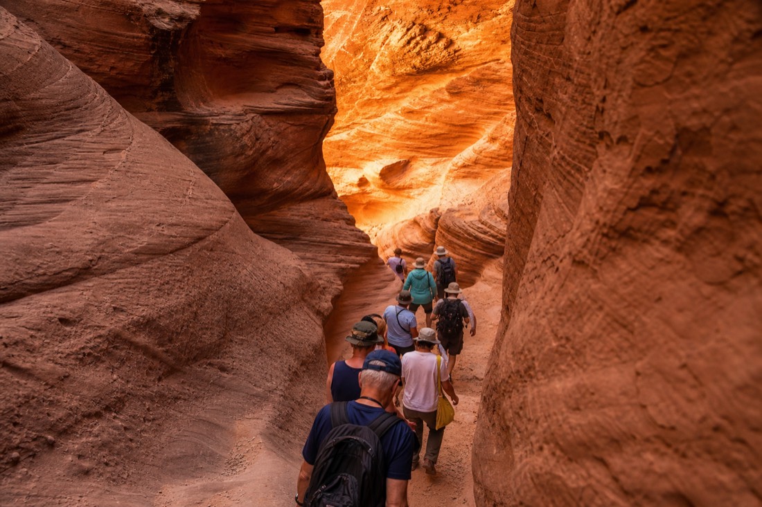 Early tour group descending into a glowing slot canyon in soft morning light
