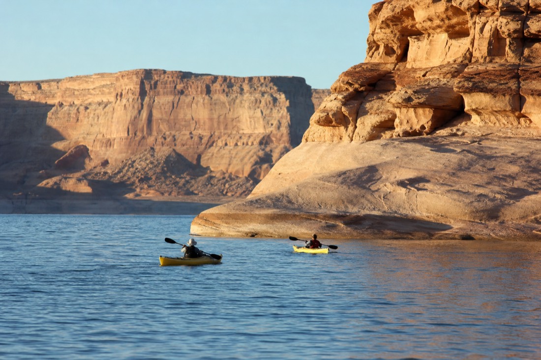 Afternoon light on Lake Powell water with kayakers near sandstone shoreline cliffs