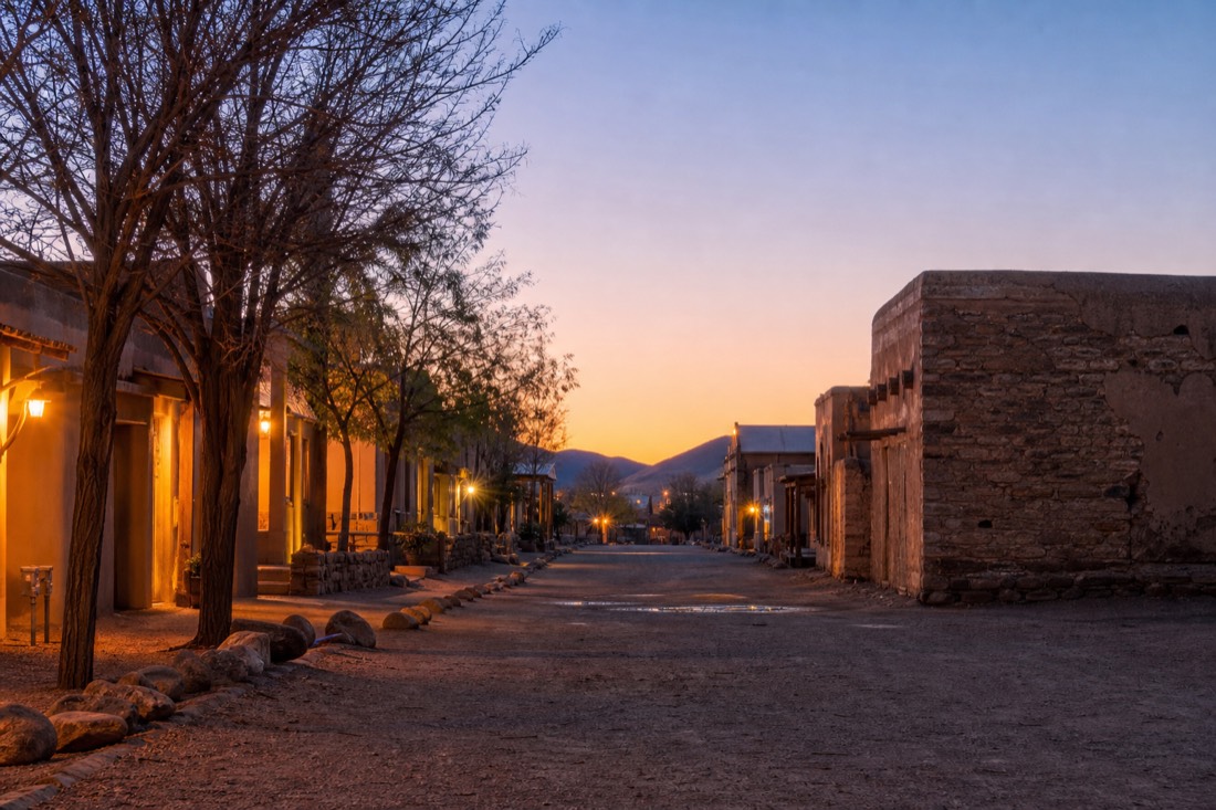 Quiet small-town street at dusk with warm lights and desert sky fading to purple
