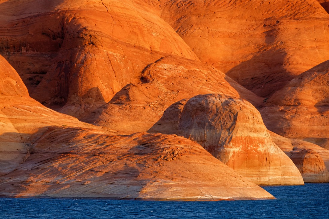 Stark otherworldly Lake Powell shoreline with bare sandstone domes meeting blue water