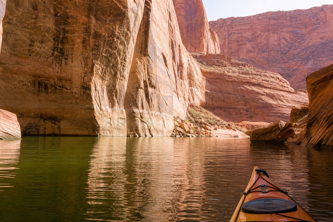 Kayaker paddling calm green water below high sandstone walls on Lake Powell