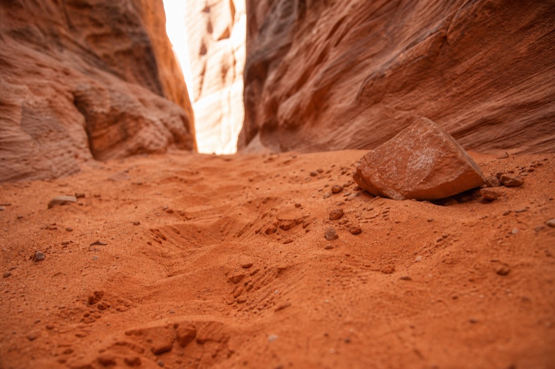 Trail running shoes stepping through deep orange sand between narrow canyon walls