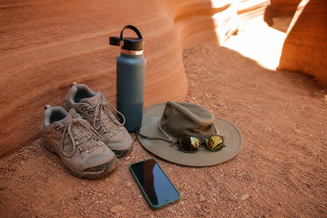 Flat lay of slot canyon essentials: shoes, water bottle, hat, sunglasses, phone