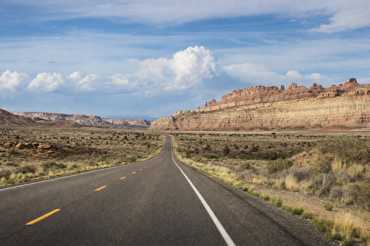 Desert highway running toward layered sandstone cliffs under a wide Southwest sky