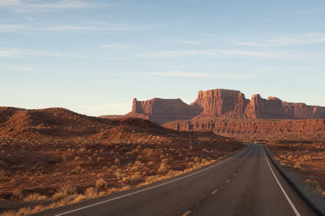 Two-lane desert road with red rock mesas in the distance on the drive toward Page