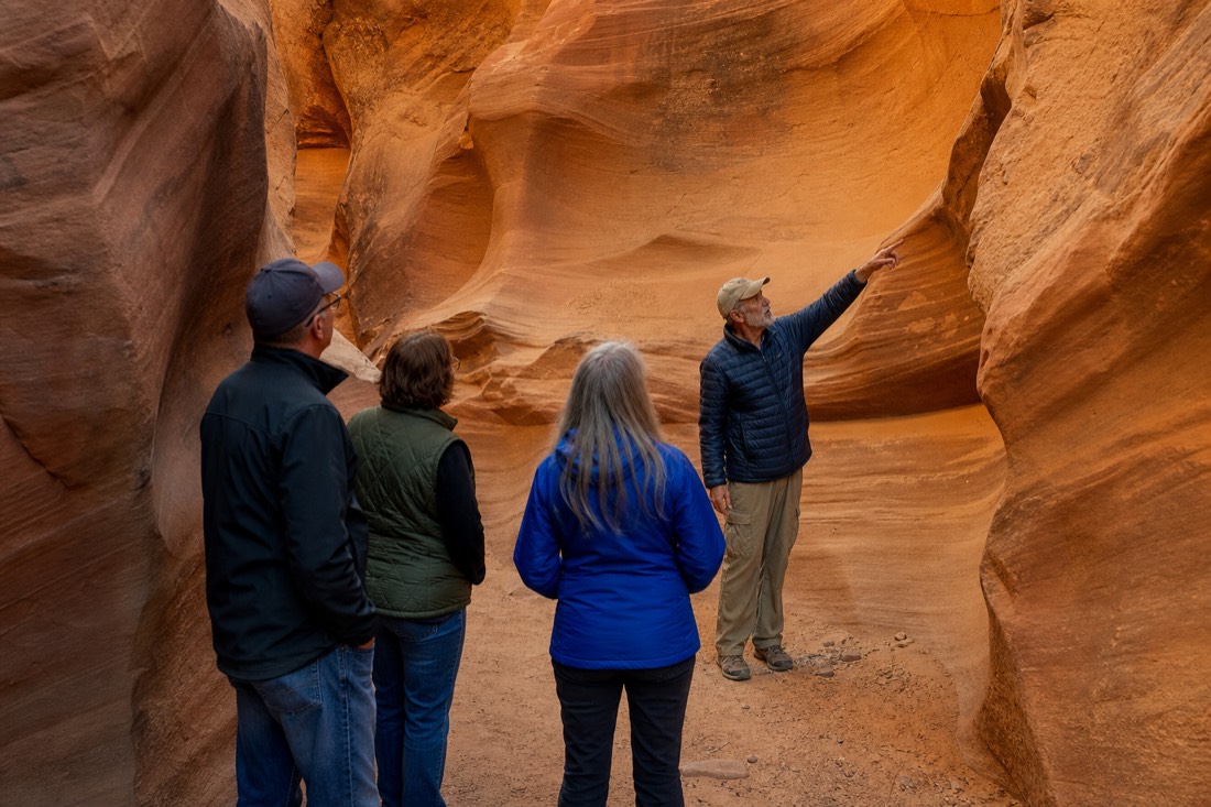 Guide gesturing toward flowing sandstone shapes while a small group listens in a slot canyon