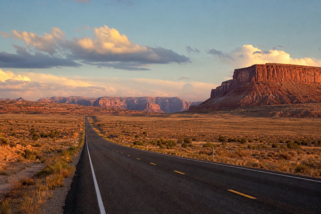 Open road at golden hour crossing Southwest desert toward far-off canyon country