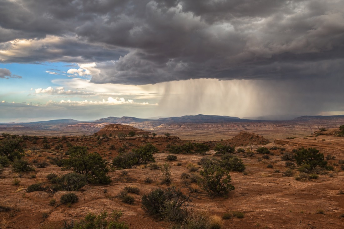Summer thunderstorm cell dropping rain over distant mesas while desert foreground stays dry