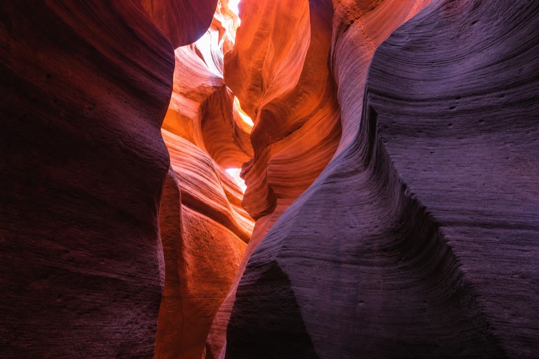 Curving layered sandstone walls glowing orange and purple inside a slot canyon
