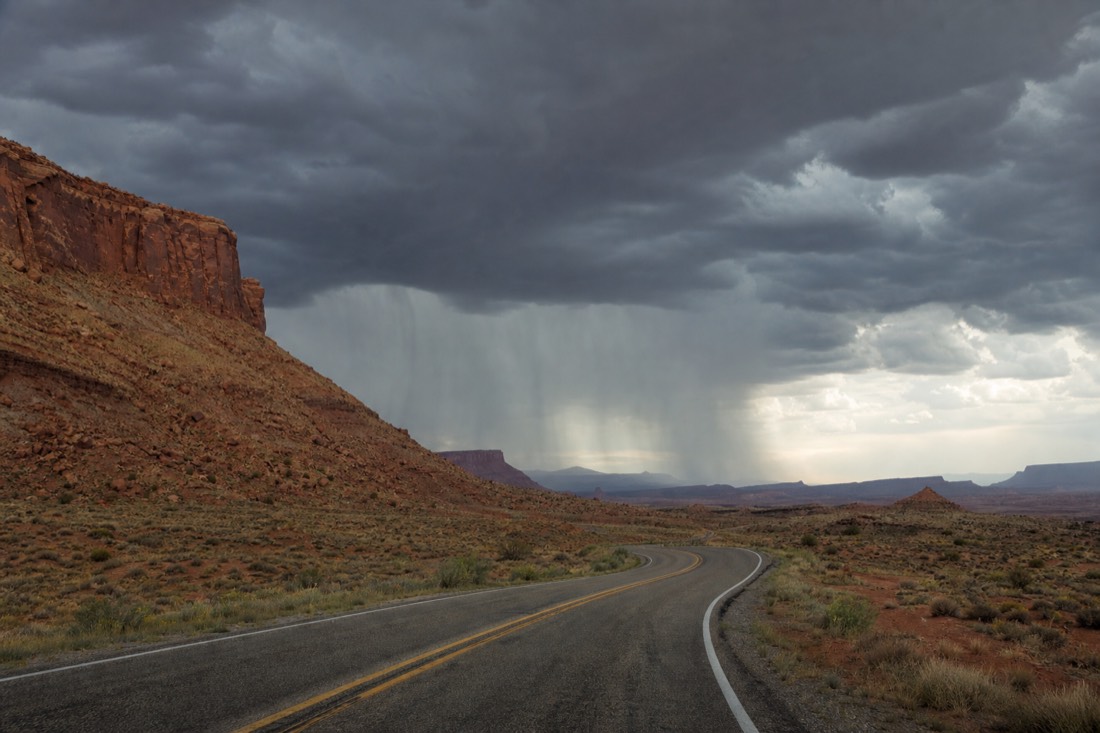 Dark storm clouds over desert highway with rain falling in the distance