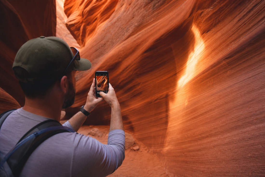 Visitor photographing a glowing slot canyon wall with a phone held steady in both hands