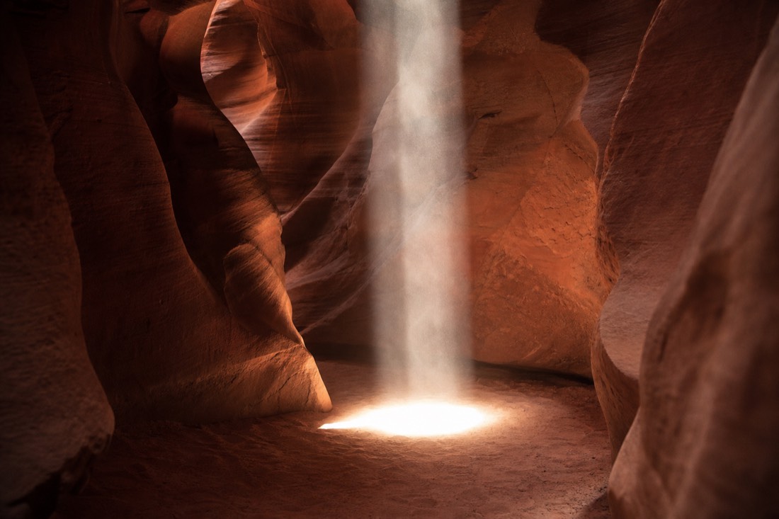 Vertical beam of sunlight striking the sandy floor of Upper Antelope Canyon at midday