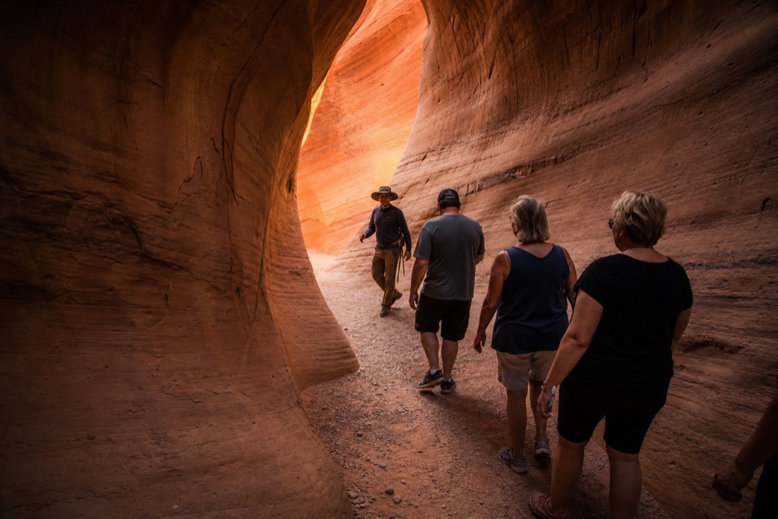 Navajo guide leading a small respectful group through a curved sandstone passage in soft light
