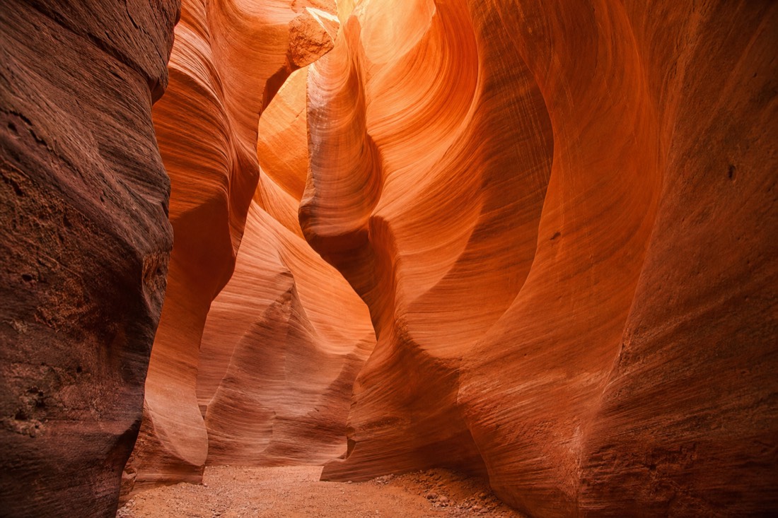 Sculpted orange slot canyon walls glowing above a sandy floor near Page Arizona