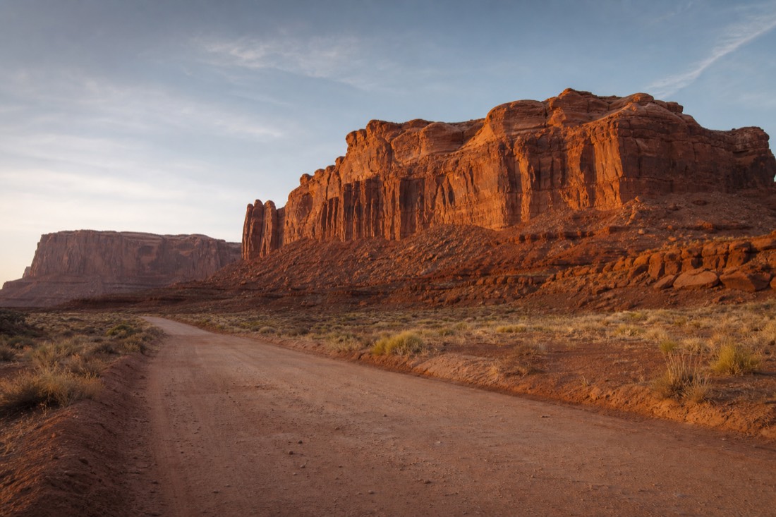 Desert entrance road to a Navajo tribal park area with red rock formations under open sky