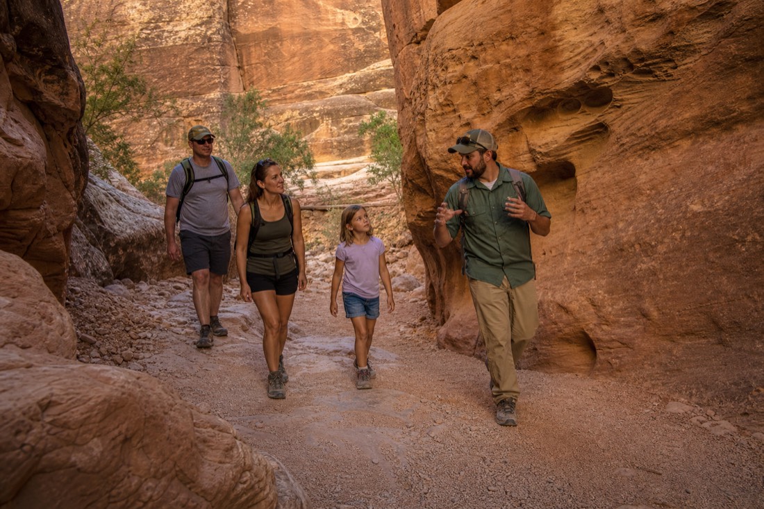 Family with a school-age child walking through a wide sunlit canyon corridor with a guide