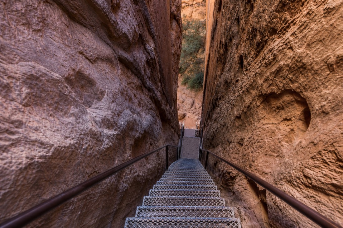 Steep metal stairway descending between narrow sandstone walls inside a slot canyon
