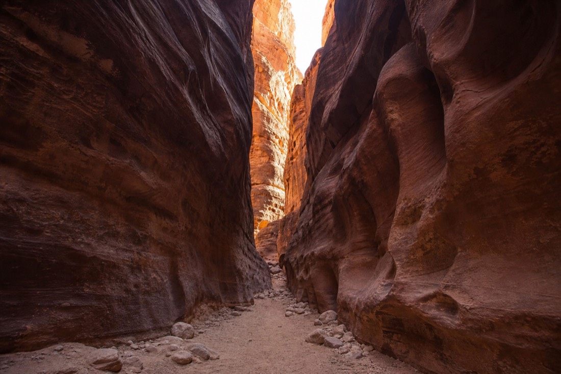 Narrow slot canyon passage open to a bright ribbon of sky far overhead