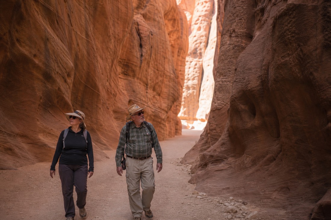 Older travelers walking comfortably through a wide flat-floored section of a glowing sandstone canyon