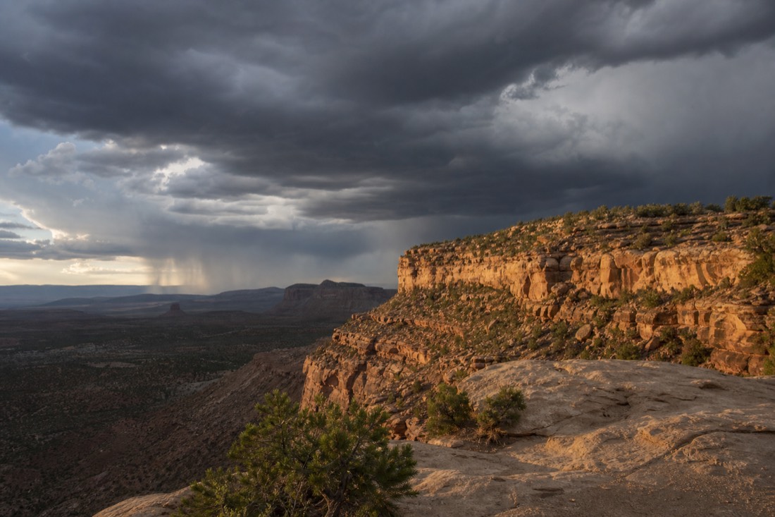 Storm clouds building over desert canyon country with rain columns visible in the distance