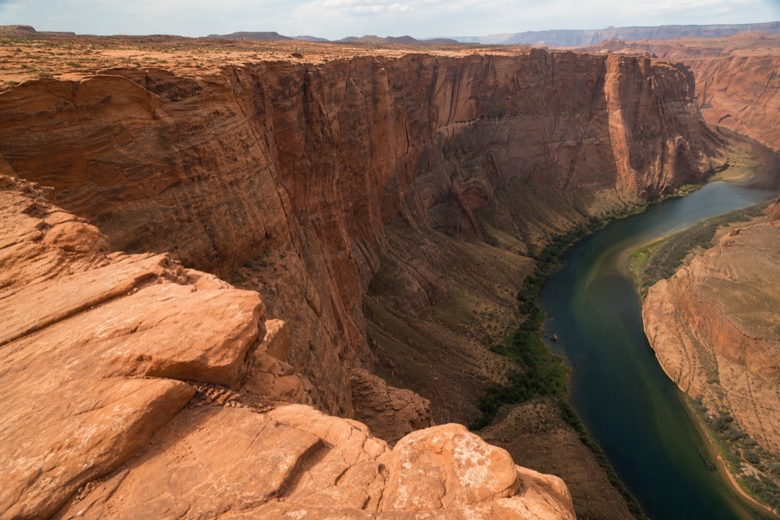 Wide bend of a green river far below sheer red canyon walls at a public overlook near Page
