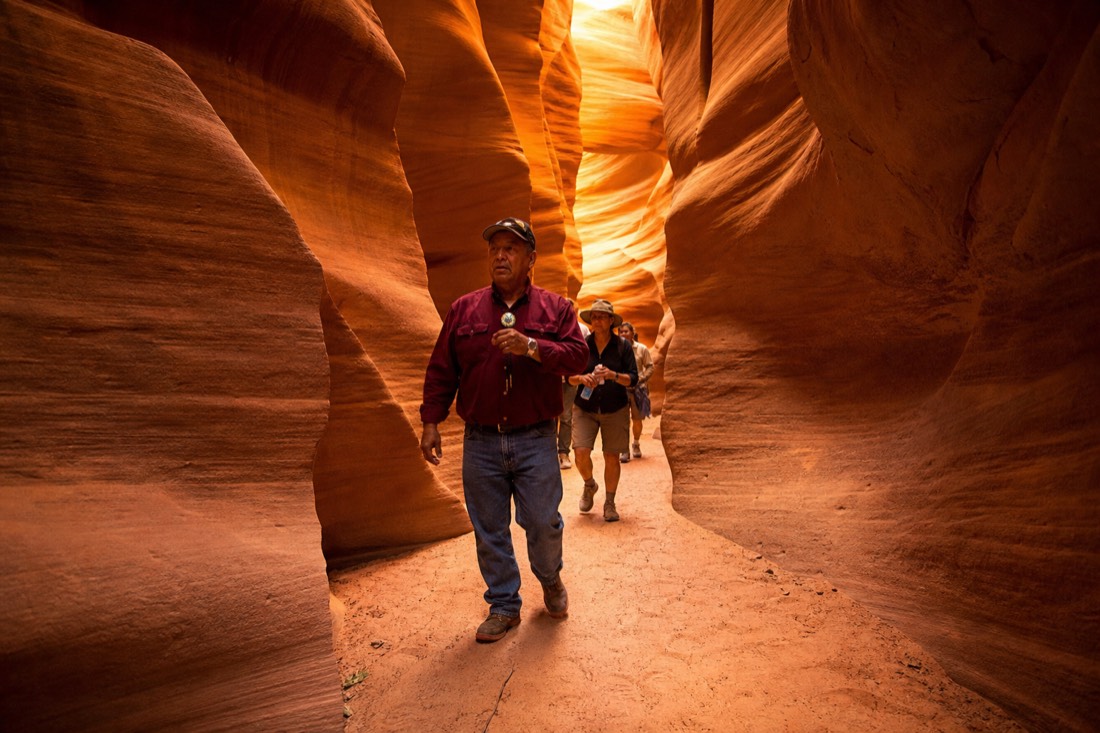 Navajo guide leading a small group along the sandy floor of a glowing slot canyon