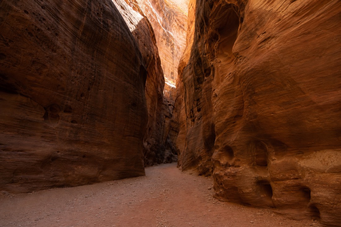 Wide sandy corridor of an A-shaped slot canyon with high sculpted walls and soft overhead light