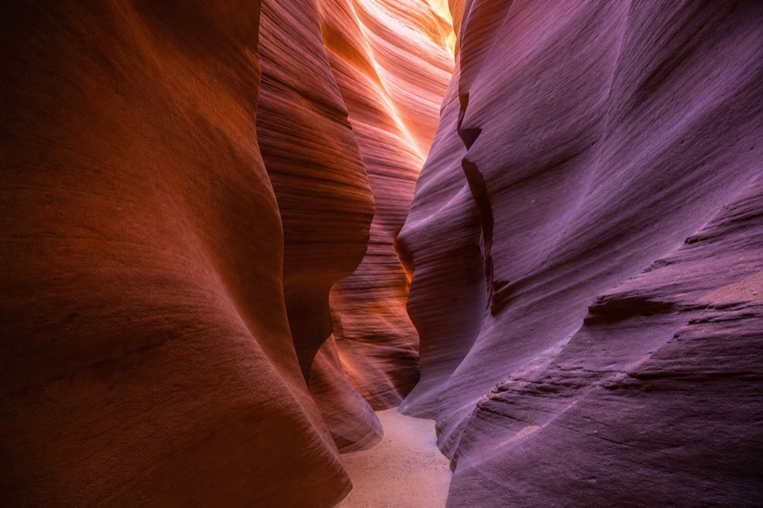 Narrow slot canyon interior with flowing sandstone curves lit in orange and violet