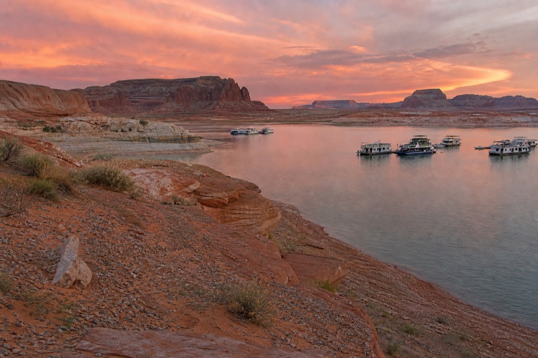 Lake Powell shoreline at dusk with houseboats and red mesas in the distance