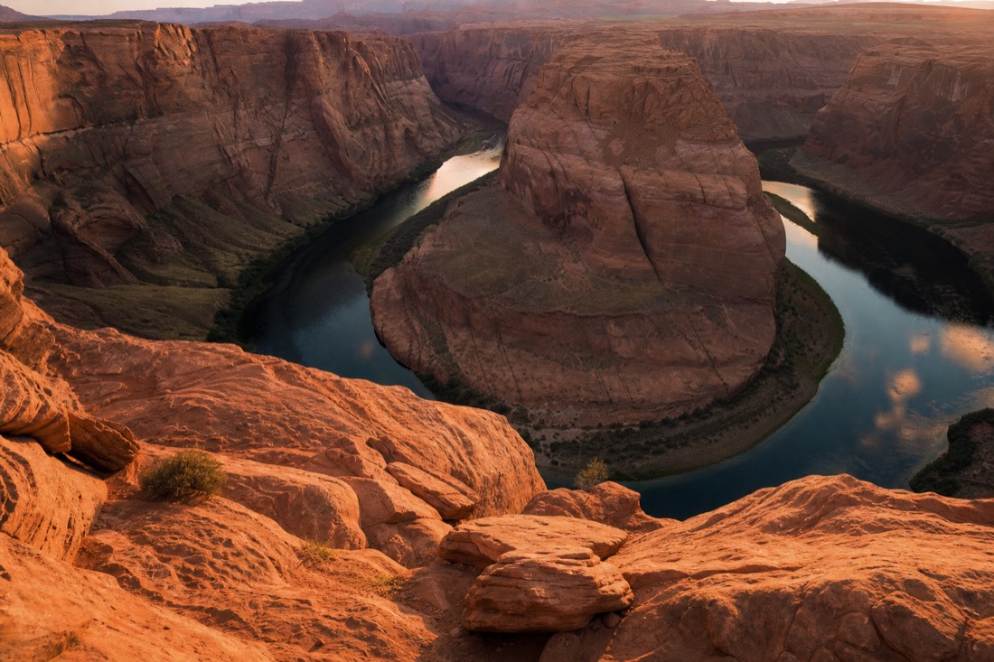 Wide bend of the Colorado River far below a sandstone rim viewpoint at golden hour