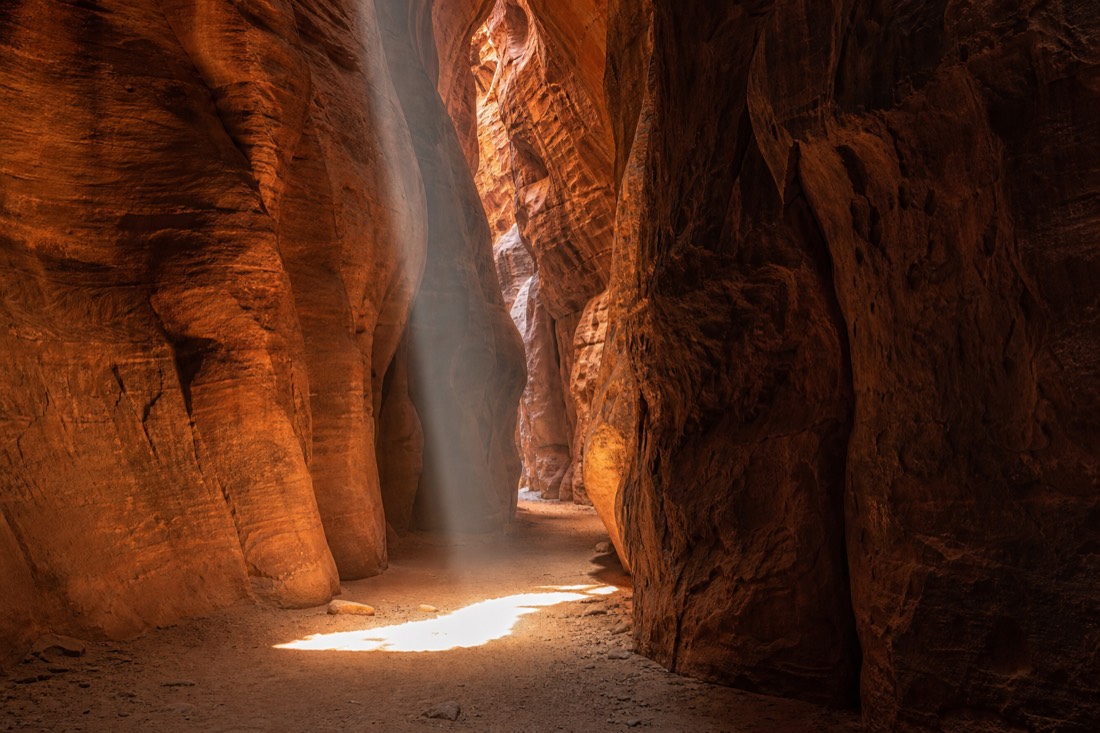 Beam of midday light striking the sandy floor of a deep sandstone slot canyon