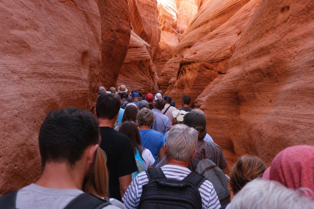 Crowded line of visitors moving through a narrow sandstone corridor in high season