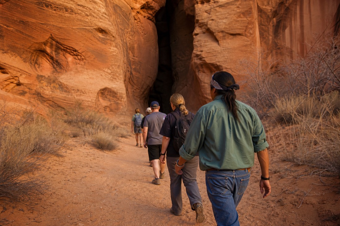 Navajo guide leading a small group across desert toward a slot canyon opening