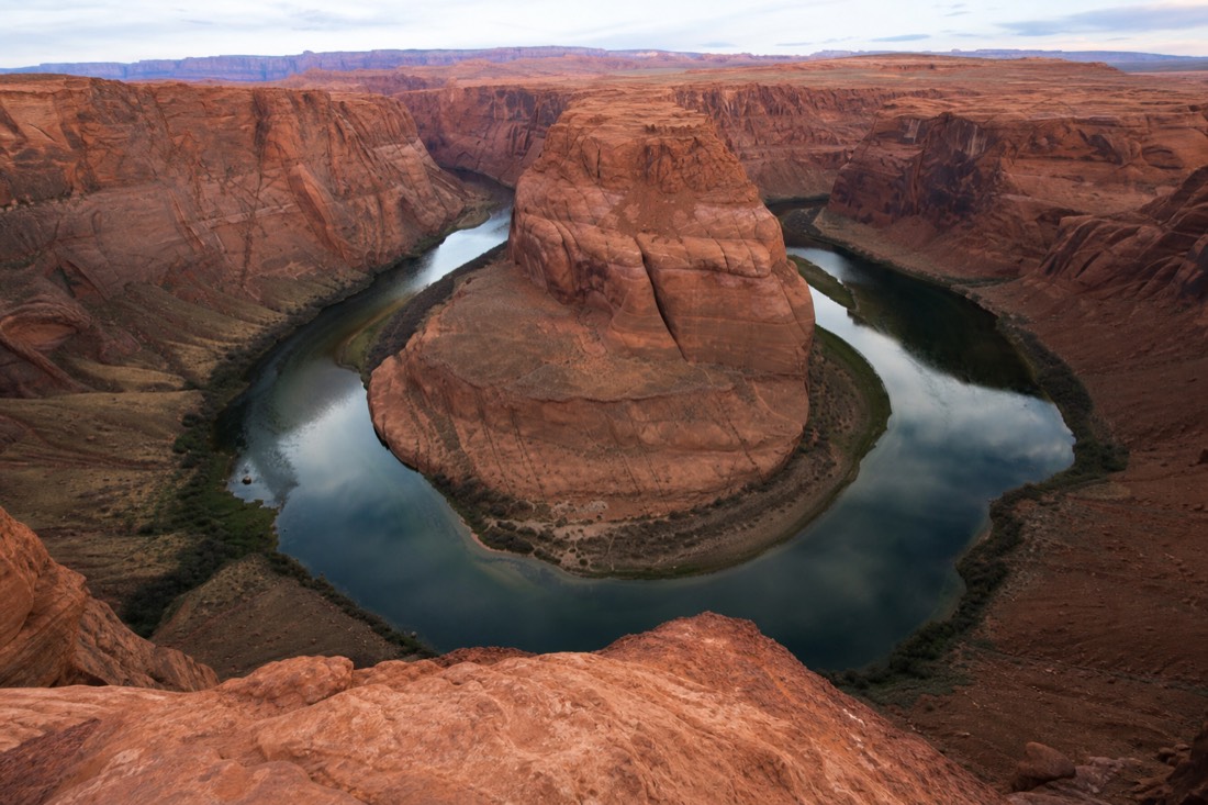 Visitors at the Horseshoe Bend rim viewpoint looking down at the emerald Colorado River