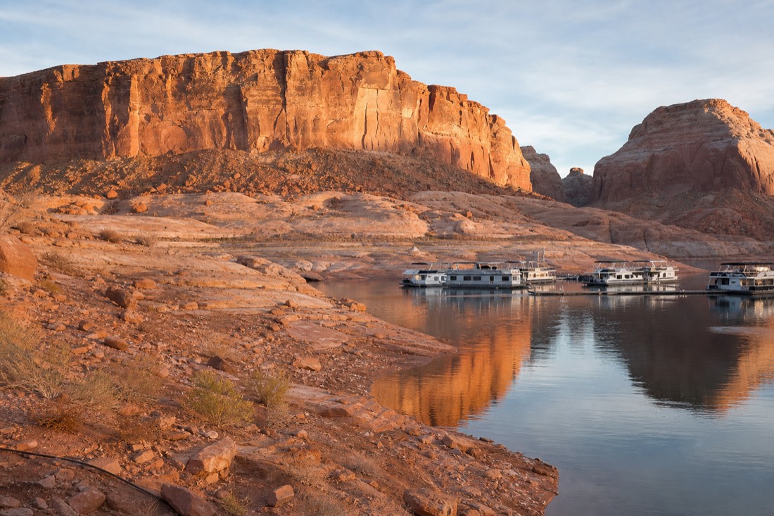 Morning light on red cliffs and calm lake water near a desert marina