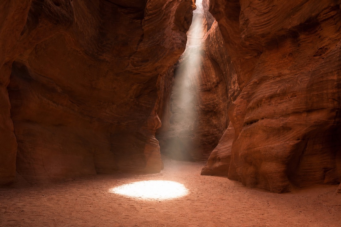 Shaft of sunlight dropping through a slot canyon opening onto the sandy floor at midday