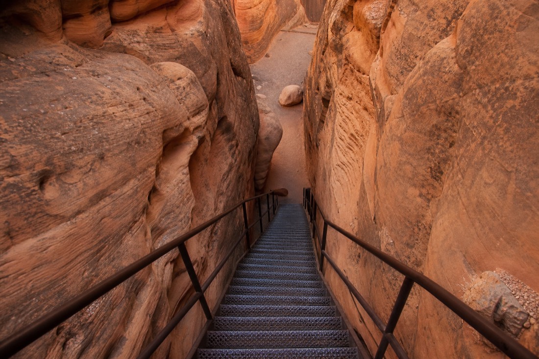 Steep metal staircase descending between narrow sandstone walls inside a slot canyon
