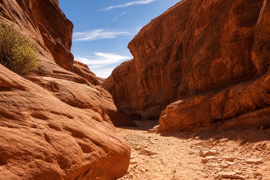 Sunlit entrance area of a desert slot canyon with warm orange rock under a blue Arizona sky