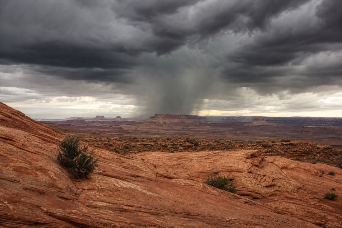 Dark monsoon storm cell dropping rain over distant mesas upstream of Antelope Canyon